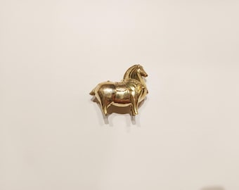 Puede incluir: Una figurita de caballo de metal de color dorado con detalles intrincados. El caballo está de pie sobre sus cuatro patas y tiene la cabeza girada hacia un lado.