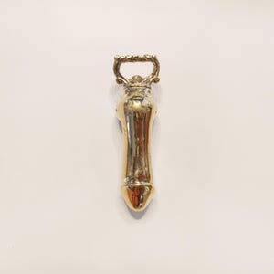 May include: A gold-colored bottle opener with a decorative handle. The opener is shaped like a bottle with a rounded top and a long, narrow neck.
