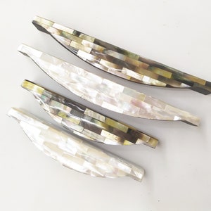 Puede incluir: Cuatro tiradores decorativos para armarios hechos de azulejos de nácar en tonos blancos, marrones y verdes. Los tiradores tienen forma de media luna.