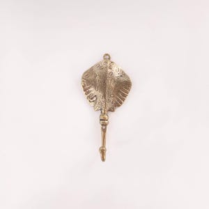 May include: A bronze-coloured metal wall hook shaped like a stingray. The hook has a detailed, textured design on the ray's body and a long, slender handle with a hook at the end. The hook is designed to be mounted on a wall.