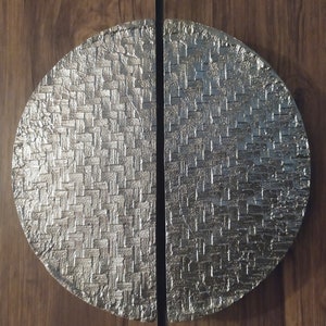 May include: A silver, round door handle with a woven pattern. The handle is split in half and mounted on a wooden door.