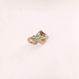 May include: A gold-colored, geometric pendant with a loop for a chain. The pendant has a unique, angular design with a polished finish. The overall shape is reminiscent of a stylized cup or vessel.