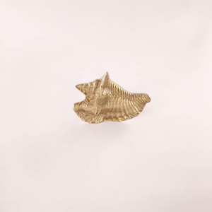 May include: A gold-coloured, seashell-shaped decorative object. The object has a textured surface with ridges and a pointed top. The seashell is set against a white background, highlighting its intricate design and form.