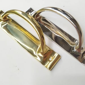 May include: Two door handles, one gold and one silver, with a curved design. The handles are mounted on a rectangular plate.