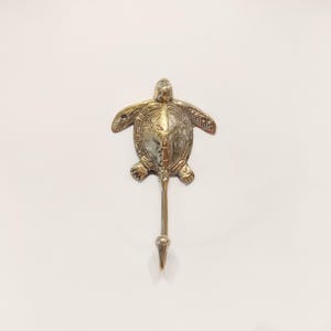 May include: A gold-colored metal turtle hook. The turtle is detailed with a textured shell and has a hook extending from its body.