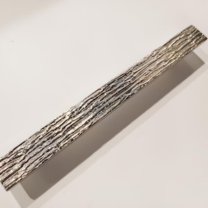 May include: A silver textured cabinet pull with a rectangular shape.