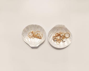 以下が含まれることがあります： 金と銀のジュエリーが入った白い貝殻の形をした2つの皿。皿は真珠層で作られており、自然で有機的な形をしています。