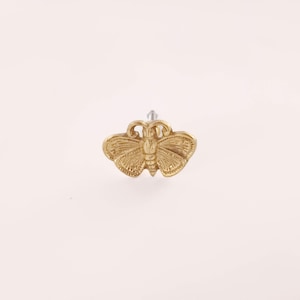 May include: A gold-colored butterfly-shaped cabinet knob. The knob features detailed wing and body patterns, and a silver screw post. The butterfly design is centered, with the wings spread out. The knob is likely made of metal.
