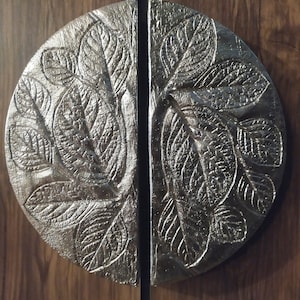 May include: A pair of silver door handles with a leaf design. The handles are made of metal and have a smooth, polished finish.