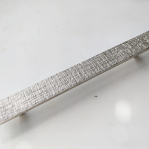 May include: A silver textured rectangular cabinet pull handle.