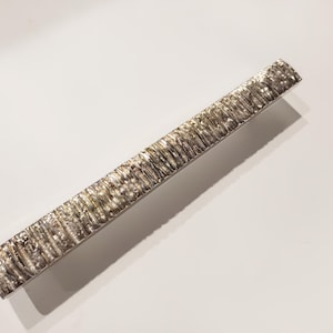 Puede incluir: Un tirador de armario plateado con una superficie texturizada y estriada.