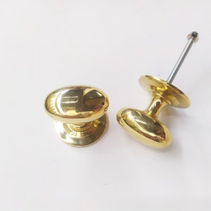 May include: Two gold oval door knobs with a polished finish. The knobs are attached to round bases.