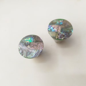 Puede incluir: Dos pomos redondos de nácar de abulón de color verde, azul y morado iridiscente. Los pomos están hechos de piezas de nácar de abulón incrustadas.