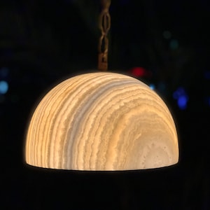 Könnte beinhalten: Eine weiße Alabaster-Pendelleuchte mit einem runden, geschichteten und strukturierten Schirm, der an einer Kette hängt.