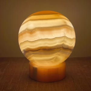 May include: A round, white and brown alabaster lamp with a striped pattern. The lamp is on a wooden surface.