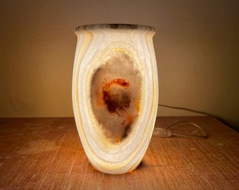 Może przedstawiać: Biała lampa z agatu z brązowym i pomarańczowym wzorem geody. Lampa jest włączona i emituje ciepłe światło.