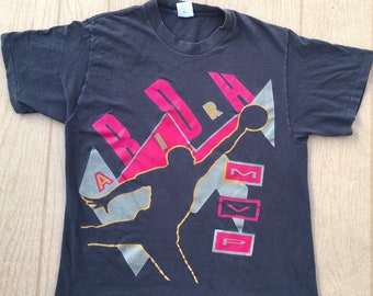 May include: Black t-shirt with a graphic print of a basketball player in silhouette, with the words "AIR" and "MVP" in gold and pink lettering.