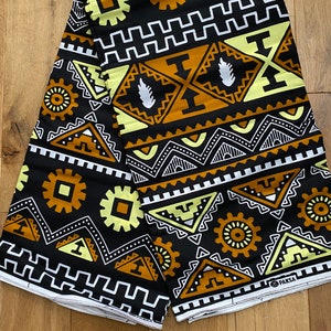 May include: Black fabric with a geometric pattern in yellow, white, and brown. The fabric has a repeating pattern of triangles, squares, and circles. The fabric is folded in half and the brand name "PAKSÁ" is visible in the bottom right corner.