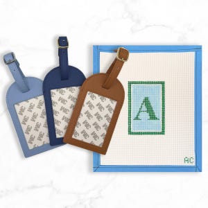 May include: Three luggage tags in light blue, navy, and brown leather, each with a buckle closure and a clear window. A canvas with a blue border and the letter "A" in green is also shown.