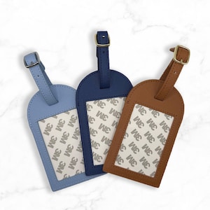 Puede incluir: Tres etiquetas de equipaje en azul claro, azul marino y marr&oacute;n. Cada etiqueta tiene una ventana rectangular con el texto "3M" repetido. Las etiquetas tienen correas a juego y hebillas doradas, dise&ntilde;adas para viajar.