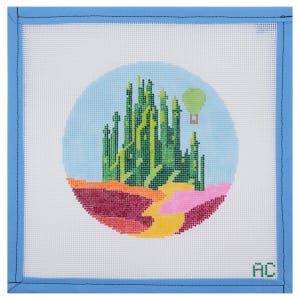 May include: Needlepoint canvas featuring a colorful scene with a green city, a hot air balloon, and a yellow road. The design is set within a light blue circle against a white background, framed by a blue border.