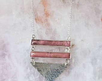 May include: A silver necklace with a triangular pendant and two rectangular pink stones. The pendant has a hammered texture.