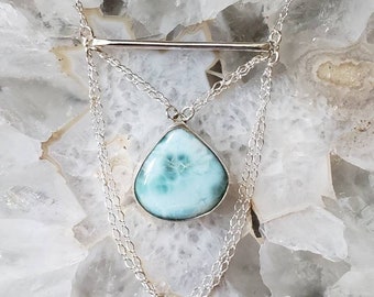 May include: A silver necklace with a blue and white gemstone pendant and a bar charm. The necklace has two chains and is layered.