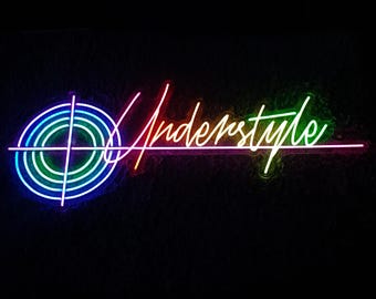 May include: A neon sign featuring a circular target graphic with concentric rings in blue, teal, and green, followed by the word Understyle in a cursive script that transitions from red to orange to yellow and green against a dark background.