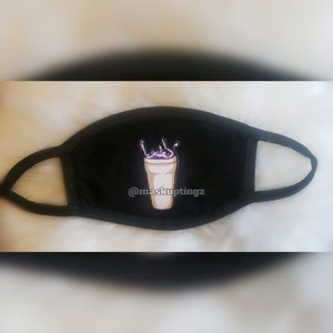 Puede incluir: Máscara facial negra con un vaso de bebida bordado en morado y blanco con el texto "@maskuptingz" en él.
