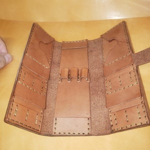 Puede incluir: Un estuche para lápices de cuero marrón con varios compartimentos y un portaplumas. El estuche está abierto y el interior es visible.