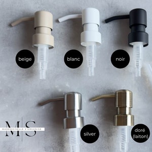 May include: Five different coloured soap pump bottles with clear tubes. The colours are beige, white, black, silver, and gold. The bottles are labelled with the colours in French.