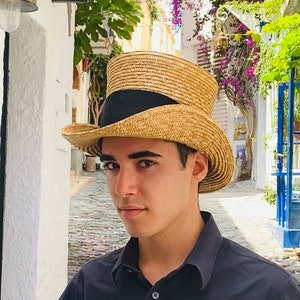 May include: A young person wearing a black button-down shirt and a straw boater hat with a black band. The hat has a tall crown and a wide brim.