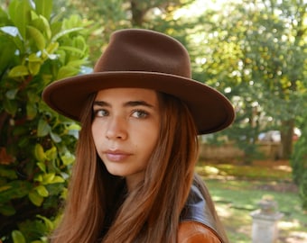 May include: A young person with long brown hair wearing a brown felt fedora hat and a brown leather jacket.