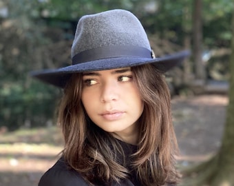 May include: A woman wearing a gray fedora with a black band and a black jacket. She is looking to the right of the frame.