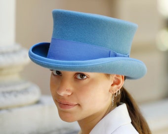 May include: A light blue top hat with a black band. The hat is worn by a person with brown hair and a nose ring.