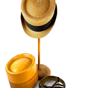 Peut inclure: Un chapeau de paille avec un ruban noir est pos&eacute; sur un support de chapeau en bois. &Agrave; c&ocirc;t&eacute; se trouve un bloc de chapeau en bois et un outil de mesure de chapeau en m&eacute;tal.
