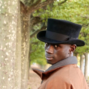 Peut inclure: Un homme portant un chapeau haut de forme noir et une veste marron. Le chapeau a un large bord et une couronne haute. L'homme regarde sur le c&ocirc;t&eacute;.