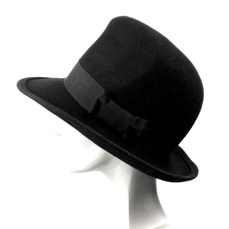 Op de afbeelding: Een zwarte wollen fedora hoed met een brede rand en een zwart lint rond de kroon.
