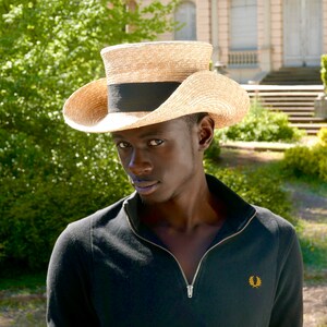 Pu&ograve; includere: Un uomo che indossa una camicia nera e un cappello di paglia a tesa larga con una fascia nera.