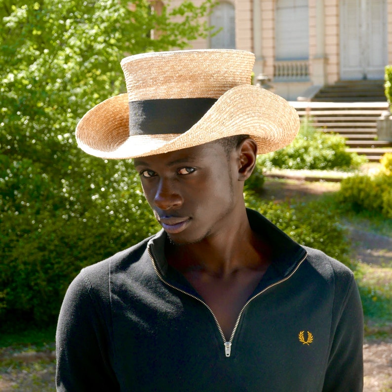 Pu&ograve; includere: Un uomo che indossa una camicia nera e un cappello di paglia a tesa larga con una fascia nera.