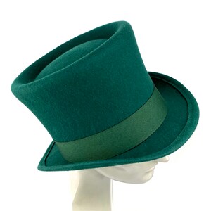 May include: A dark green felt top hat with a matching green ribbon band. The hat is angled on a white mannequin head.
