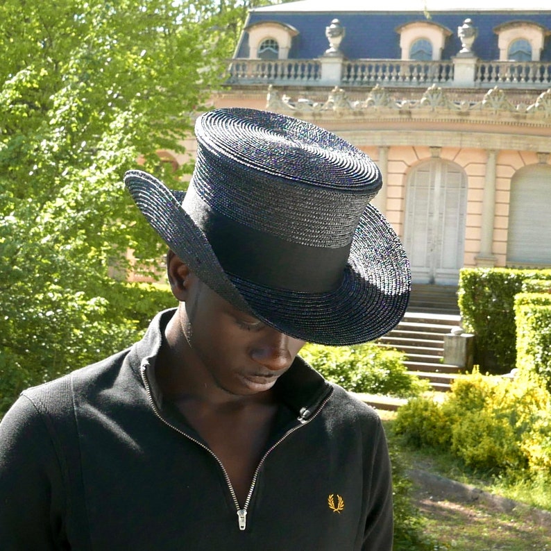 May include: A black top hat with a wide brim and a black band. The hat is made of a woven material and has a slightly textured surface.