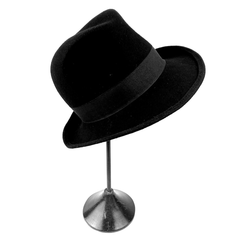 Op de afbeelding: Een zwarte fedora hoed met een zwarte lintband, getoond op een zwarte metalen standaard.