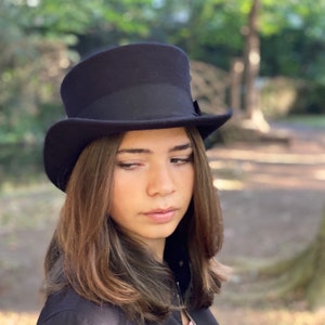 May include: A black top hat with a wide brim and a black band around the crown. The hat is worn by a person with long brown hair.