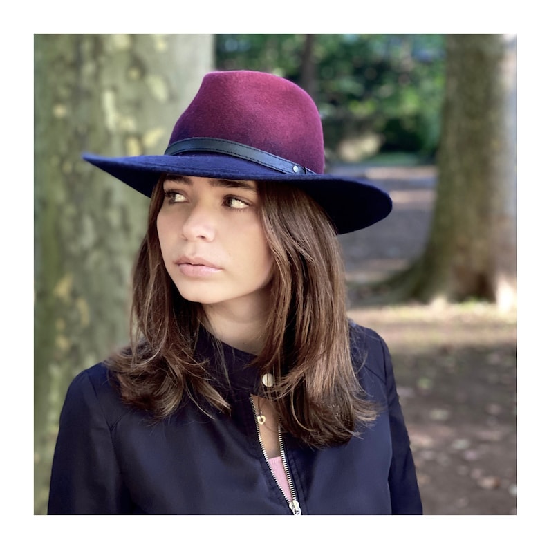 May include: A burgundy and black felt fedora hat with a black leather band. The hat is worn by a person with long brown hair.