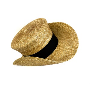 Pu&ograve; includere: Un cappello di paglia a tesa larga con un nastro nero attorno alla corona. Il cappello &egrave; fatto di un materiale di paglia intrecciata e ha una tesa leggermente arricciata.