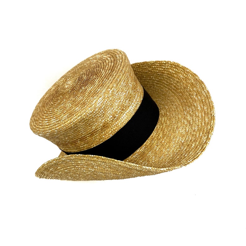 Pu&ograve; includere: Un cappello di paglia a tesa larga con un nastro nero attorno alla corona. Il cappello &egrave; fatto di un materiale di paglia intrecciata e ha una tesa leggermente arricciata.