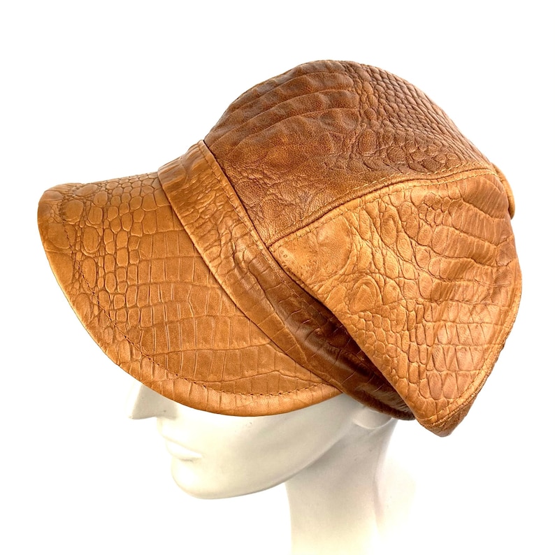 May include: A brown leather hat with a crocodile pattern. The hat has a wide brim and a curved crown.