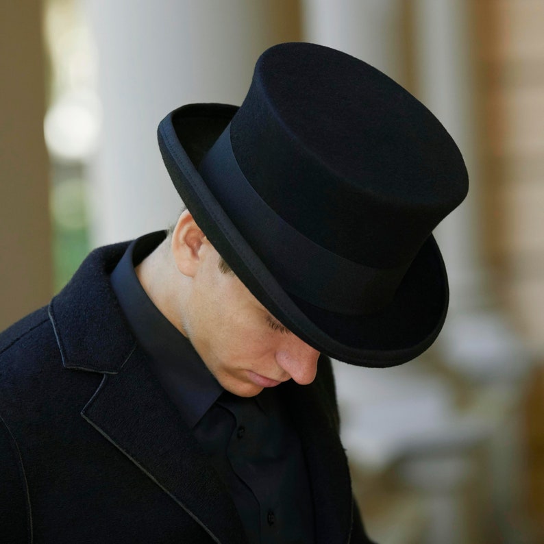May include: A black top hat with a black band. The hat is made of felt and has a tall, cylindrical crown.