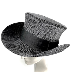May include: A black top hat made of woven straw with a black grosgrain ribbon band. The hat has a wide brim and a tall crown.